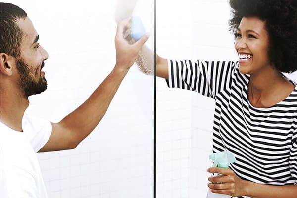 Man and woman cleaning opposite sides of a glass panel while smiling and laughing at each other.