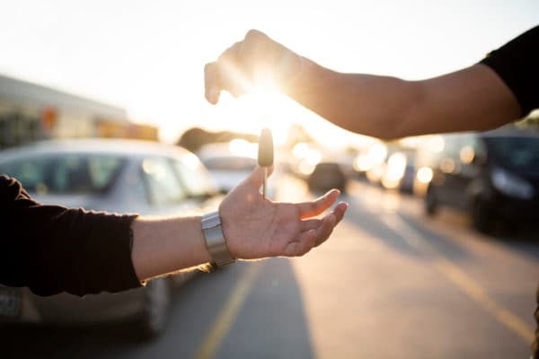 A man handing his car key over to another man to let him borrow his vehicle.