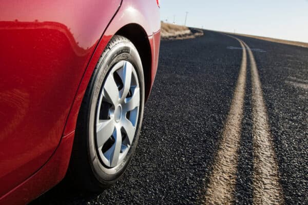 Close up of a rear tire of a red car as it drives down a street.